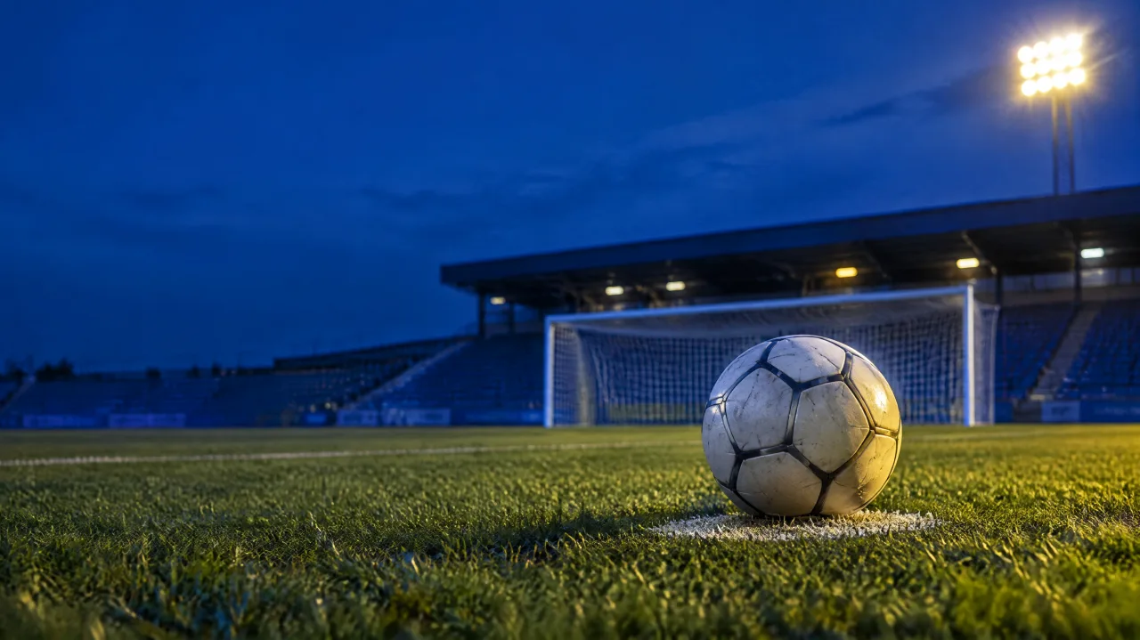 Bola de futebol sobre a marca do pênalti, com o gol ao fundo em um campo iluminado ao entardecer